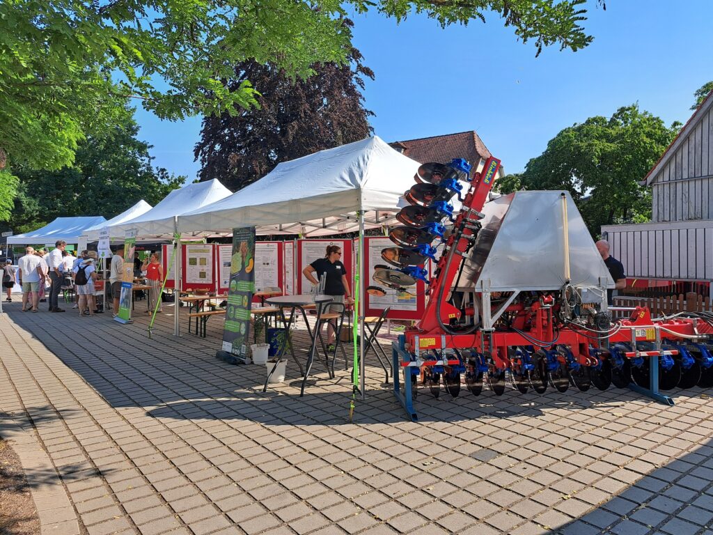 Unser Foto zeigt den Stand des Biomasse-Instituts am Johannitag 2026. Im Vordergrund ist das Ausstellungsstück Injektionsdüngungsgerät des Projekts "LiqInject" zu sehen.