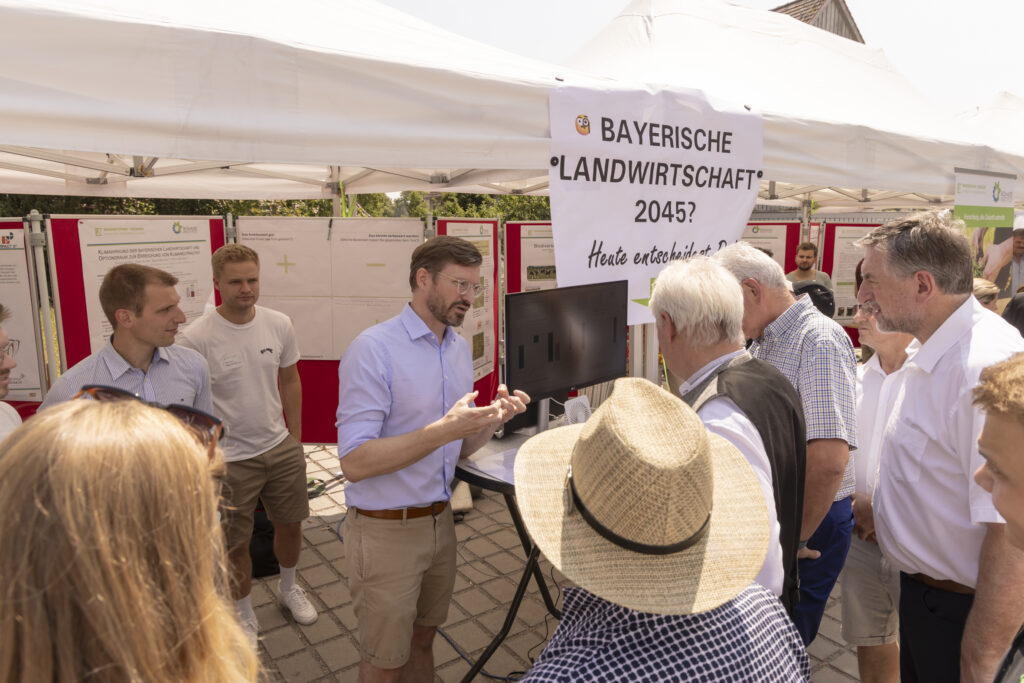 Unser Foto zeigt den Ehrengast Bundesminister für Landwirtschaft, Ernährung und Heimat, Alois Rainer (CSU) am Stand des Biomasse-Instituts im Gespräch mit forschenden Professuren und Mitarbeitenden des Biomasse-Institut.