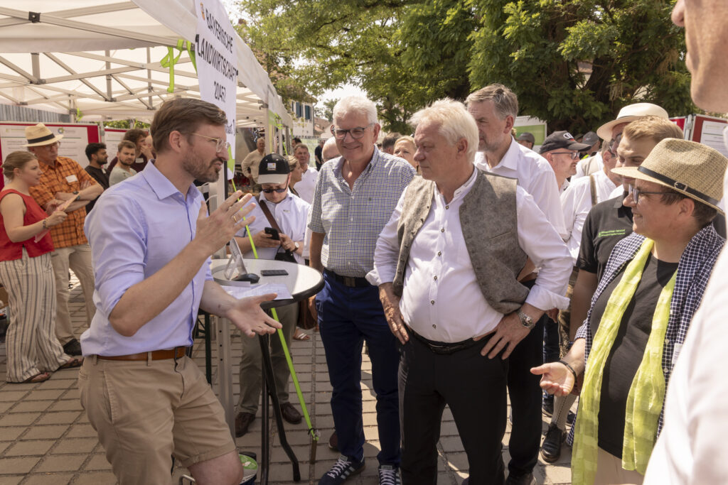 Unser Foto zeigt den Ehrengast Bundesminister für Landwirtschaft, Ernährung und Heimat, Alois Rainer (CSU) am Stand des Biomasse-Instituts im Gespräch mit forschenden Professuren und Mitarbeitenden des Biomasse-Institut.