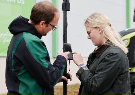 Ein Mann und eine Frau stehen an einem Vermessungsstab und bedienen diesen.