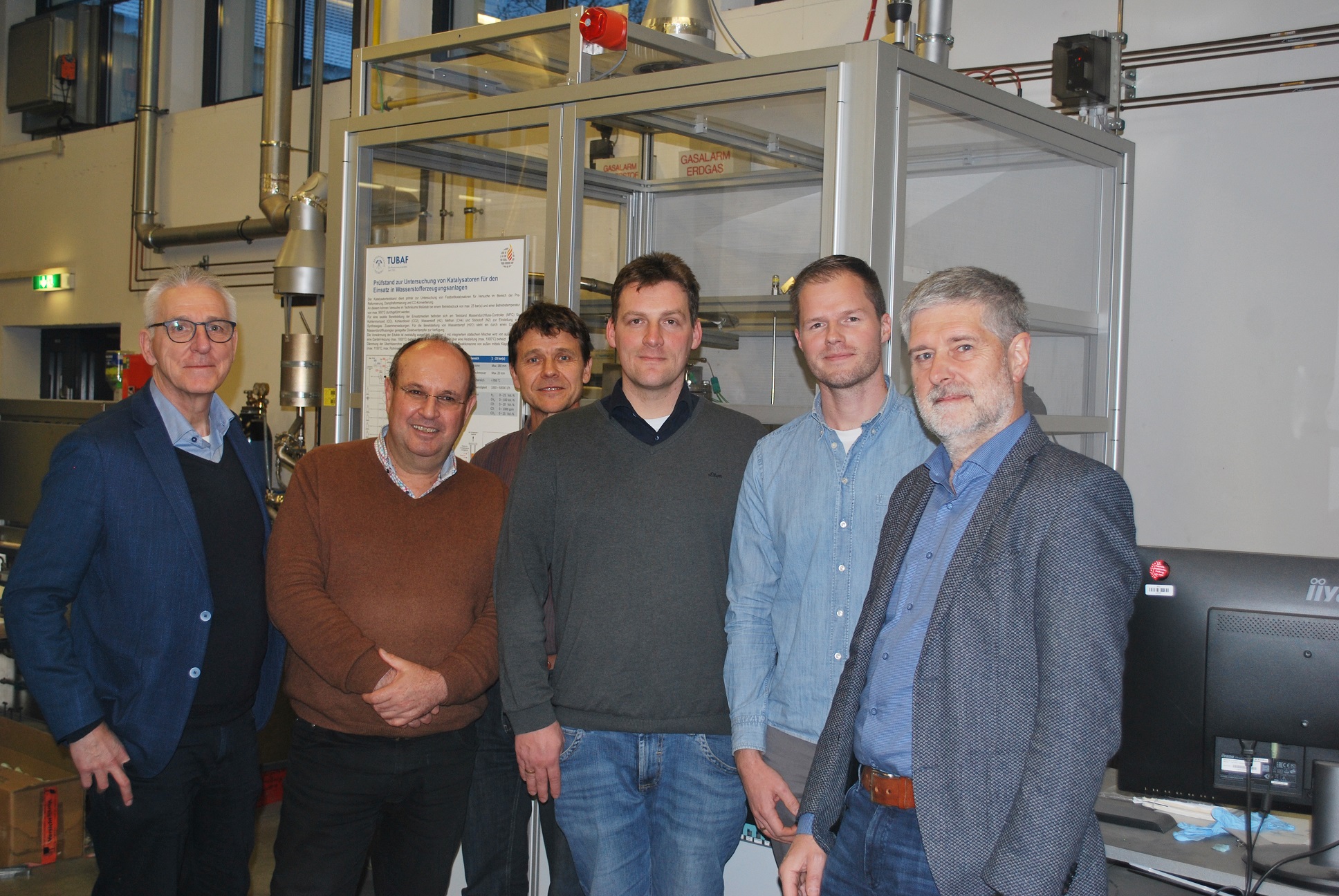 Unser Foto zeigt: Zusammenarbeit für erneuerbare Energien: Projektteam BioRED vor dem Biogas-Reformer der TU Bergakademie Freiberg (von links nach rechts) • Jörg Kapischke (Professor, Hochschule Ansbach) • Alfons Himmelstoß (AEV Energy, Geschäftsführender Gesellschafter AEV) • Erik Ferchau (Wissenschaftlicher Mitarbeiter, Gas- und Wärmetechnische Anlagen, TU Bergakademie Freiberg) • Johannes Fichtner (Wissenschaftlicher Mitarbeiter, Hochschule Ansbach) • Jan Ninow (Wissenschaftlicher Mitarbeiter, Hochschule Ansbach) • Hartmut Krause (Professor, Gas- und Wärmetechnische Anlagen, TU Bergakademie Freiberg)