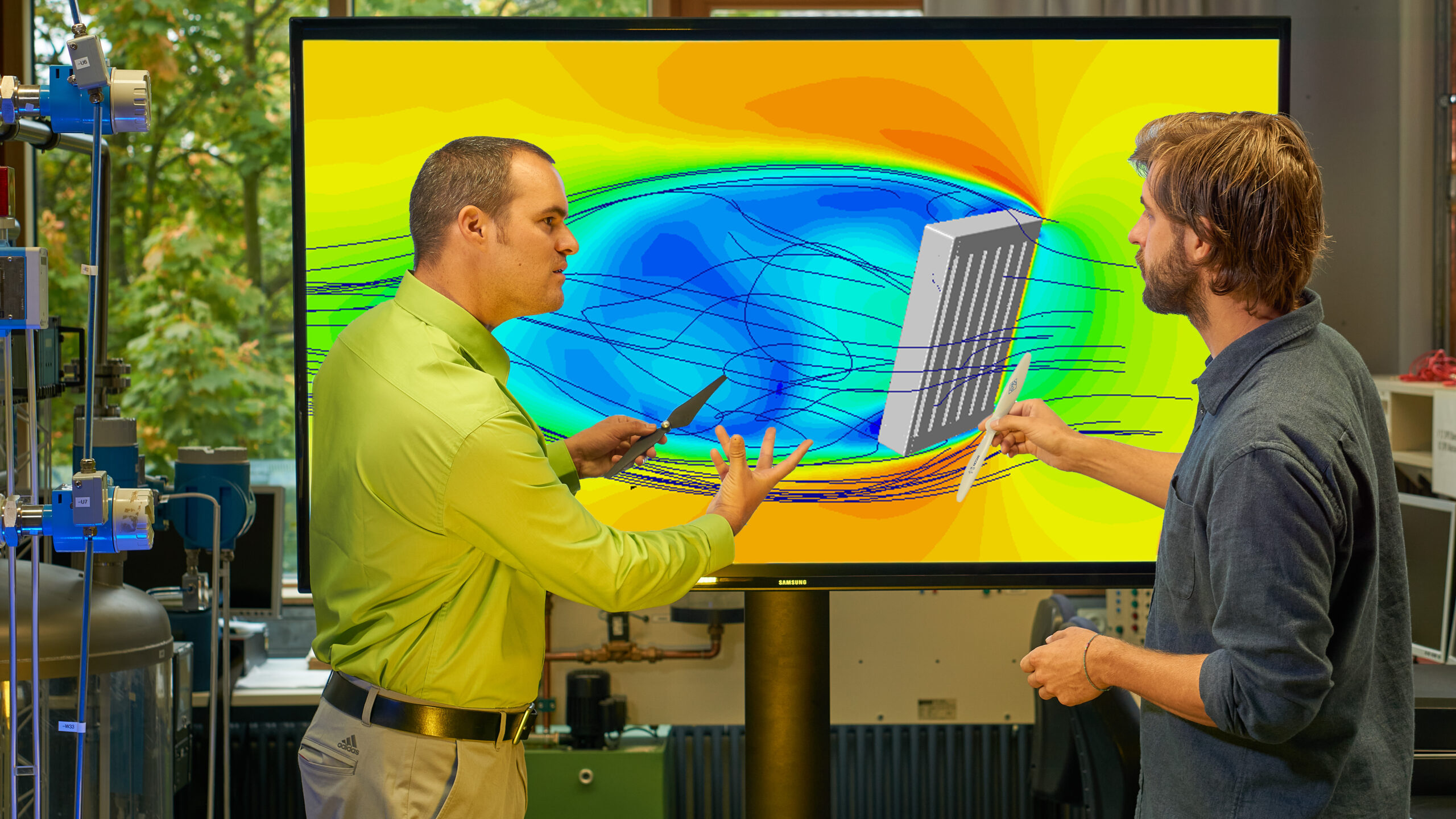 Die zwei Personen stehen vor einem einem Monitor auf welchem in verschiedenen Farben und Linien die Strömungen in einer Biogasanlage, die durch ein Rührwerk verursacht werden, dargestellt sind.