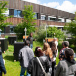 Unser Foto zeigt den BIT-Mitarbeitenden Matthias Wörlein steht vor Versuchsständen auf dem Campus Triesdorf und spricht zum Publikum. Beim Rundgang über den Campus informierten sich die Gäste zu den Themen Nachhaltigkeit und Ökologie. Unter anderem präsentierte der wissenschaftliche Mitarbeiter und Alumnus Matthias Wörlein das Forschungsprojekt Climate4Roofs. © Mechthild Müller
