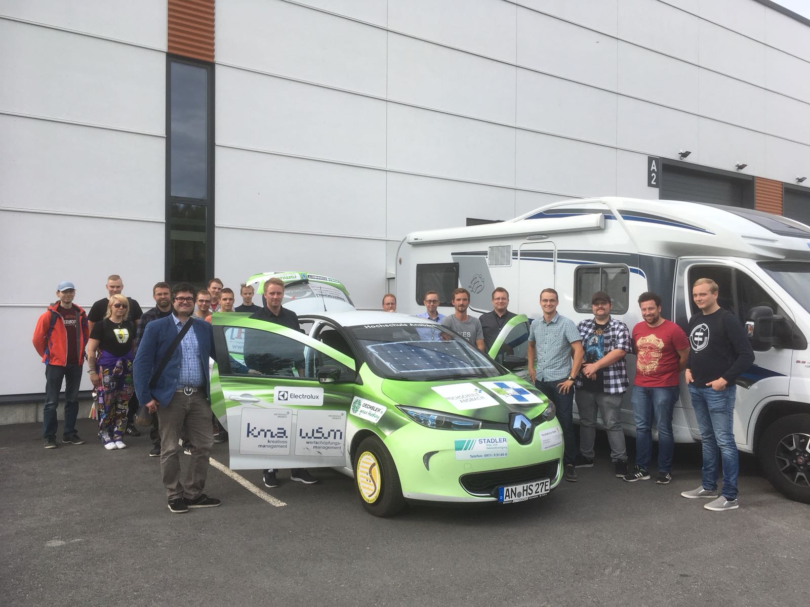 Um das grüne Forschungsauto aus Ansbach sind jede Menge Menschen (18) versammelt, die Türen vorne und der Kofferaum stehen offen