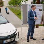 Dr. Gerd Müller mit Prof. Norbert Huber unterhalten sich neben dem Triobrid, dahinter ein Plakat zum Triobrid